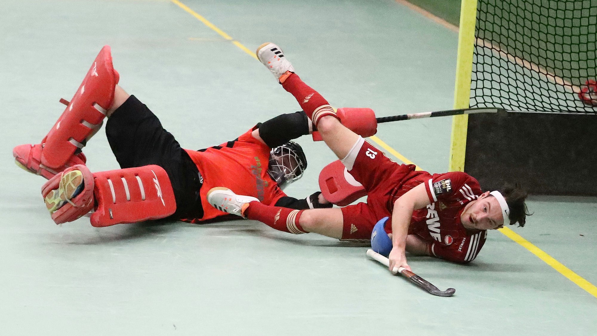 Ein Hockeytorwart und ein Feldspieler liegen am Boden und kämpfen um den Ball.