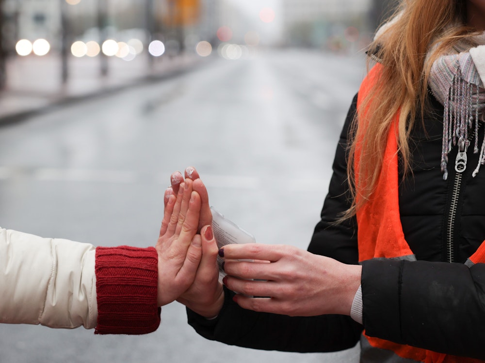 Klimaaktivisten sitzen mit ihren Händen zusammengeklebt auf einer Straße am Potsdamer Platz und wärmen sich ihre Hände mit einem Wärmekissen.