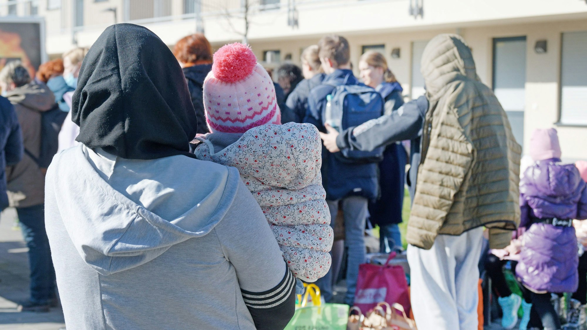 Geflüchtete aus der Ukraine stehen mit ihrem Gepäck vor den Gebäuden eines Flüchtlingsheims in Köln-Worringen.