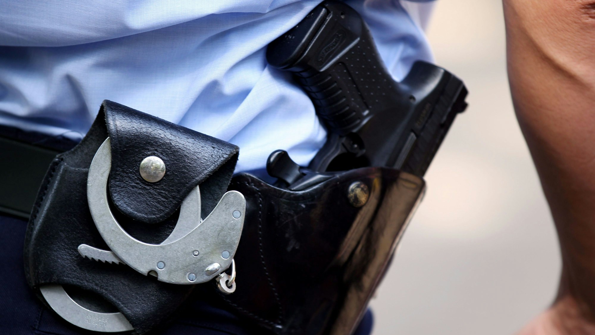Ein Polizist mit Handschellen und Pistole am Gürtel steht auf einem Schulhof.