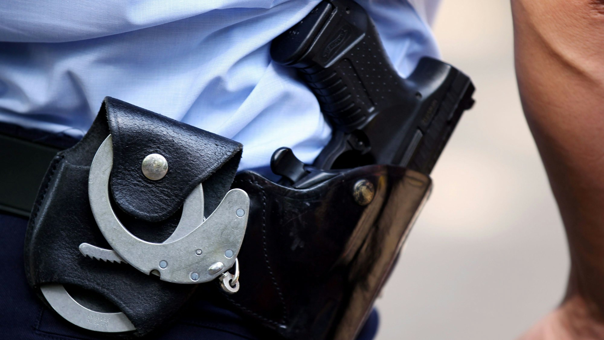 Nordrhein-Westfalen, Köln: Ein Polizist mit Handschellen und Pistole am Gürtel steht in Köln auf einem Schulhof.