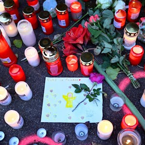 Kerzen und Blumen stehen an einem Tatort, an dem am Tag zuvor zwei Mädchen von einem Mann mit einem Messer angegriffen wurden. In der Mitte ist ein gemaltes Bild von einem Engel, über dem „Ruhe in Frieden“ steht.&nbsp;