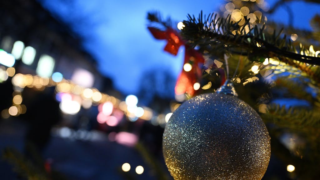 Das Symbolfoto zeigt eine goldene Weihnachtsbaum-Kugel, im Hintergrund sind Tannengrün und Lichter zu sehen.