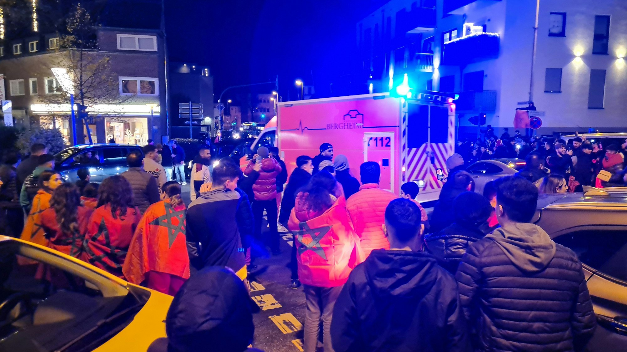 Fußballfans der marokkanischen Nationalmannschaft stehen auf einer Kreuzung, ein Rettungswagen mit Blaulicht versucht hindurch zu kommen.