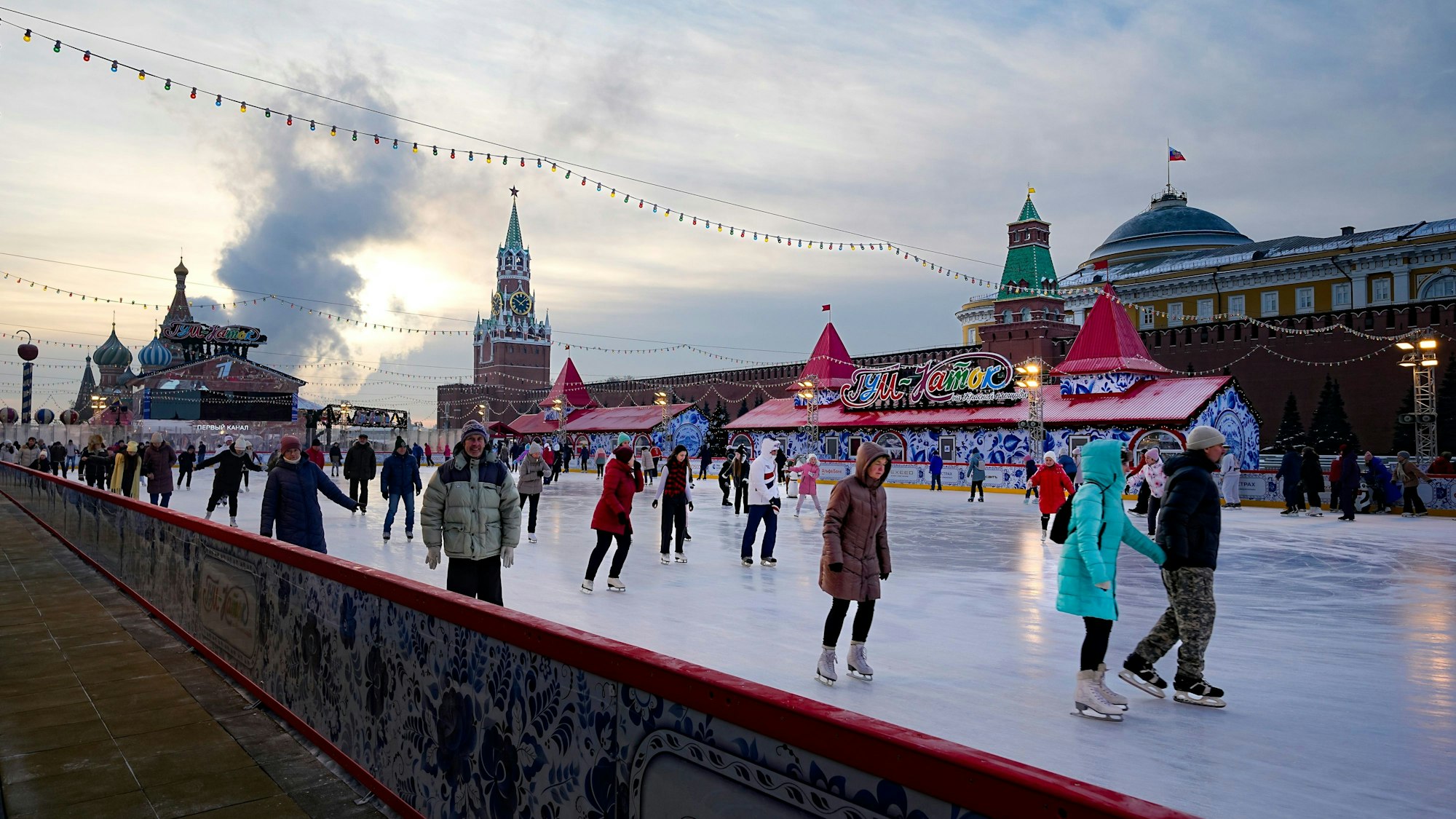 Russland, Moskau: Menschen laufen Anfang Dezember 2022 Schlittschuh auf der Eisbahn auf dem Roten Platz, der für die Weihnachts- und Neujahrsfeierlichkeiten geschmückt ist, während im Hintergrund die Kreml-Mauer zu sehen ist.
