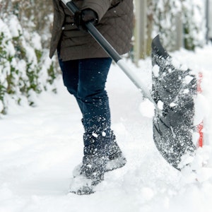 Eine Frau räumt mit einer Schneeschaufel den Schnee beiseite, um ihrer Räumpflicht nachzukommen.