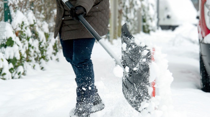 Eine Frau räumt mit einer Schneeschaufel den Schnee beiseite, um ihrer Räumpflicht nachzukommen.