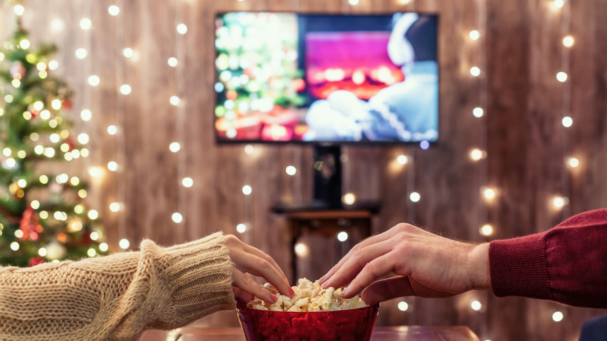 Eine Frau und ein Mann greifen nach Popcorn, während sie einen Film gucken.