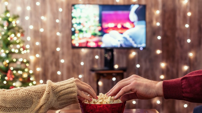 Eine Frau und ein Mann greifen nach Popcorn, während sie einen Film gucken.