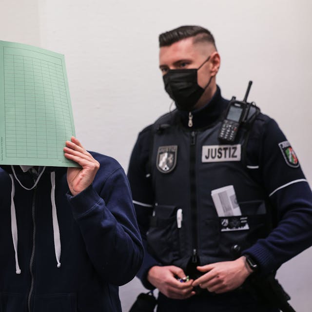 Der Angeklagte (M.) im Missbrauchskomplex Wermelskirchen hält sich beim Betreten des Gerichtssaals neben seinem Rechtsanwalt Christian Lange (l) eine Mappe vor das Gesicht.