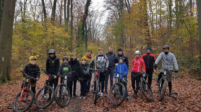 Eine Gruppe Mountainbiker steht mit ihren Rädern im Wald.