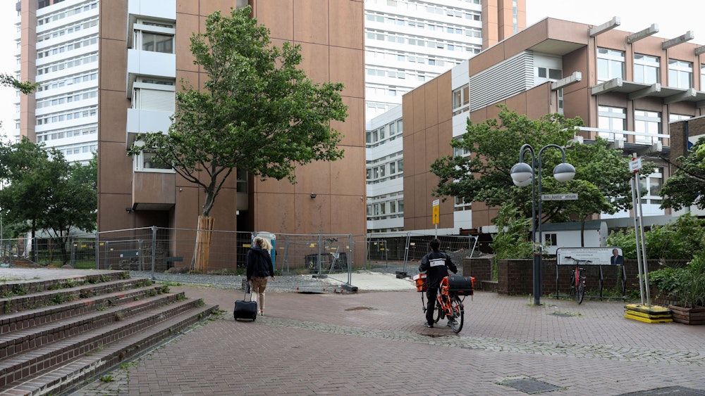 Eine Frau geht mit einem Koffer am Kölner Gericht entlang. Dort ist eine Baustelle zu sehen.
