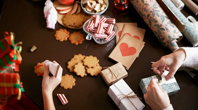 Mutter und Kind sitzen am Tisch, dekorieren Kekse und verpacken Geschenke.
