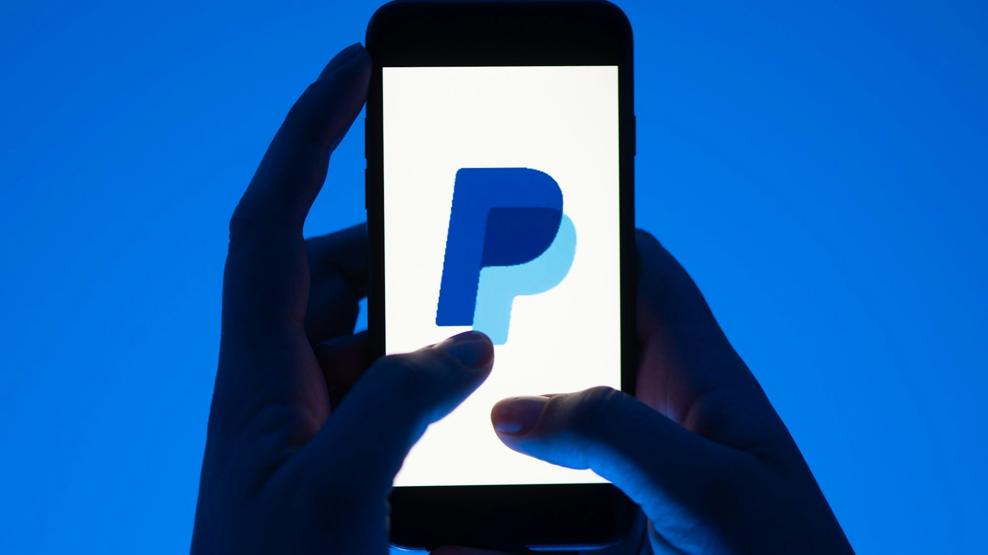 Eine Frau hält ein Smartphone mit dem Logo des Bezahldienst Paypal in der Hand.