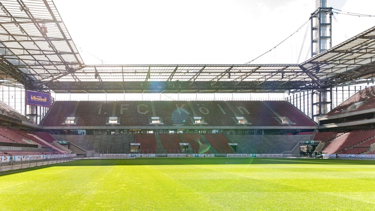 Innenansicht des Rhein-Energie-Stadions in Köln. Die Zuschauerplätze sind leer, die Sonne scheint.