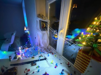 Lego-Figuren sind auf einer weißen Fläche, die eine Schneelandschaft sein soll, arrangiert. Eine Lego-Seilbahn schwebt über der Szenerie.