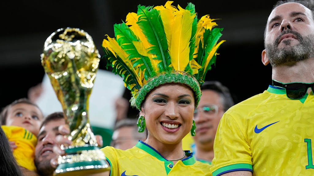 Eine Frau im Brasilien-Outfit hält bei der WM 2022 im Stadion eine Attrappe des Weltmeister-Pokals in die Kamera.