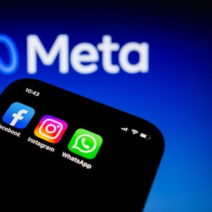 Die Apps von Facebook, Instagram und WhatsApp sind auf einem Smartphone vor dem Logo von Meta Platforms zu sehen.