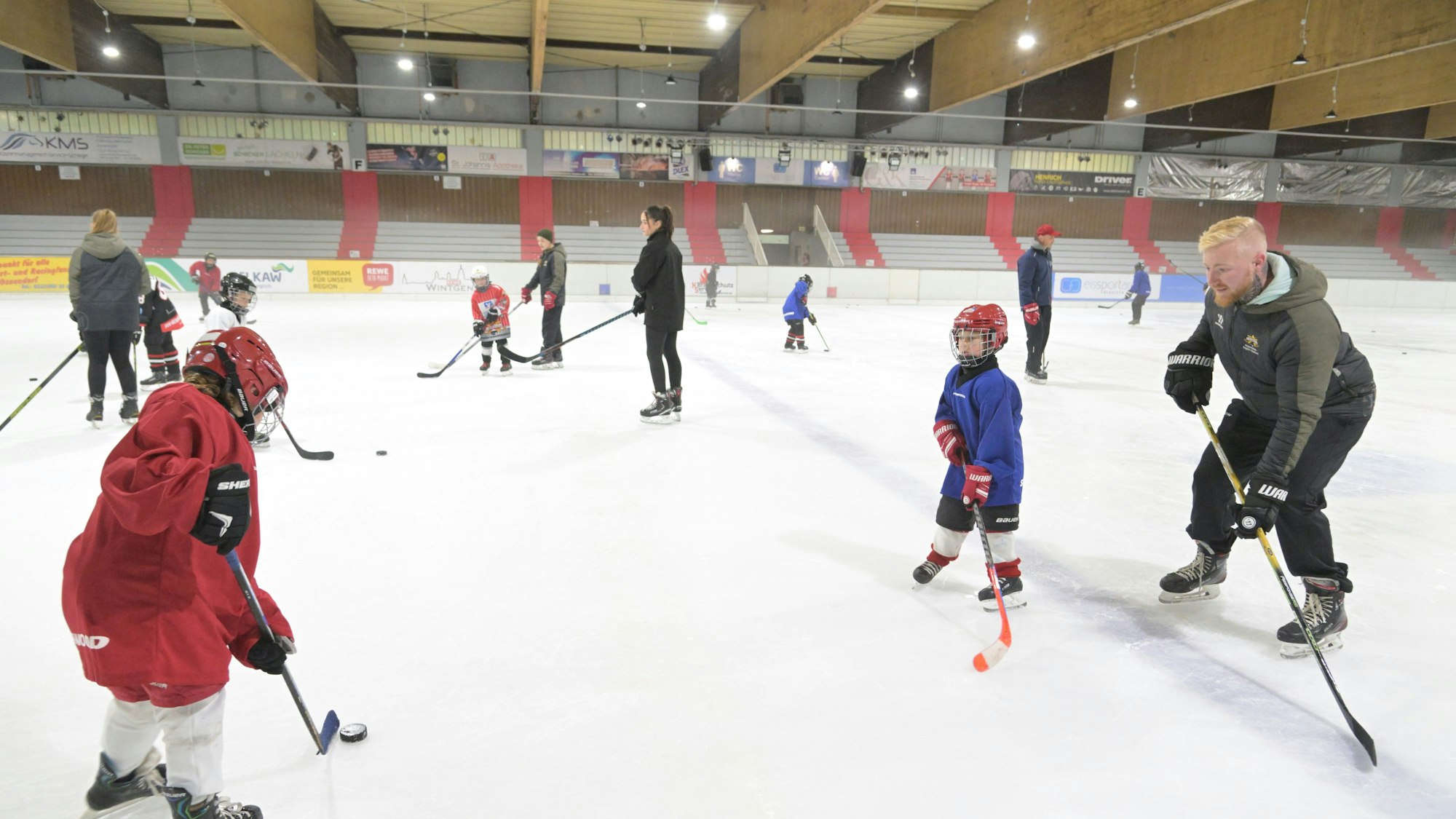 Auf dem Eis in der Halle trainiert eine Kinder-Eishockey-Mannschaft mit ihren Trainern.