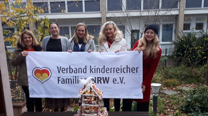 Fünf Frauen halten ein Transparent hoch mit dem Schriftzug Verband kinderreicher Familien NRW e.V. Auf einer Bank davor steht ein liebevoll verziertes vier Etagen hohes Lebkuchenhaus.&nbsp;