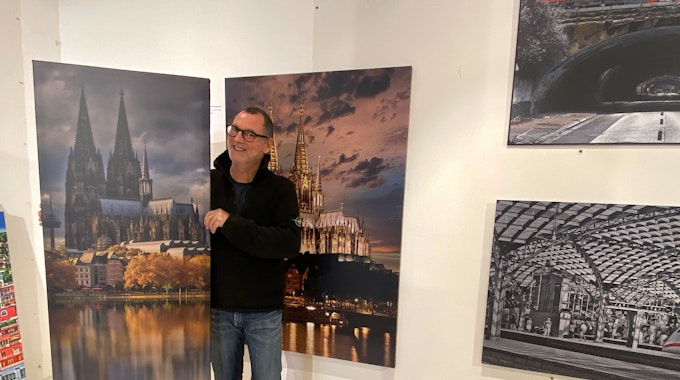 Ein Mann in einer schwarzen Jacke steht rechts rechts vor dem Bild in einer Galerie. Das Gemälde zeigt den Kölner Dom mit seiner Spiegelung im Wasser