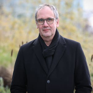 Bestseller-Autor Volker Kutscher steht vor dem Neven DuMont-Haus. Er trägt einen schwarzen Mantel und einen schwarzen Schal.