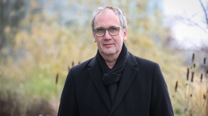 Bestseller-Autor Volker Kutscher steht vor dem Neven DuMont-Haus. Er trägt einen schwarzen Mantel und einen schwarzen Schal.