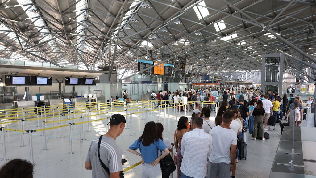 Menschen warten in einer großen Schlange am Flughafen Köln/Bonn an der Sicherheitskontrolle.