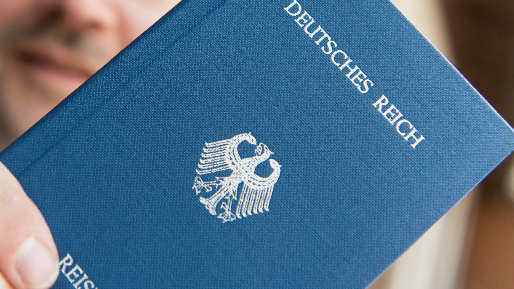 Ein Mann hält ein Heft mit dem Aufdruck «Deutsches Reich Reisepass» in der Hand.