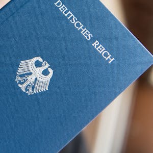 Ein Mann hält ein Heft mit dem Aufdruck „Deutsches Reich Reisepass“ in der Hand.
