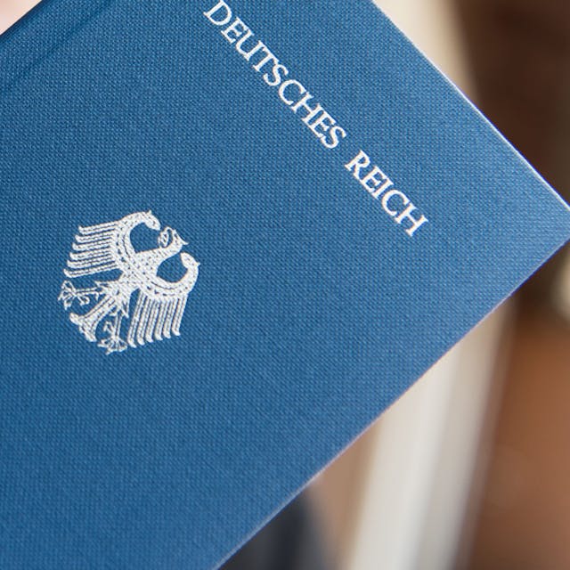 Ein Mann hält ein Heft mit dem Aufdruck „Deutsches Reich Reisepass“ in der Hand.