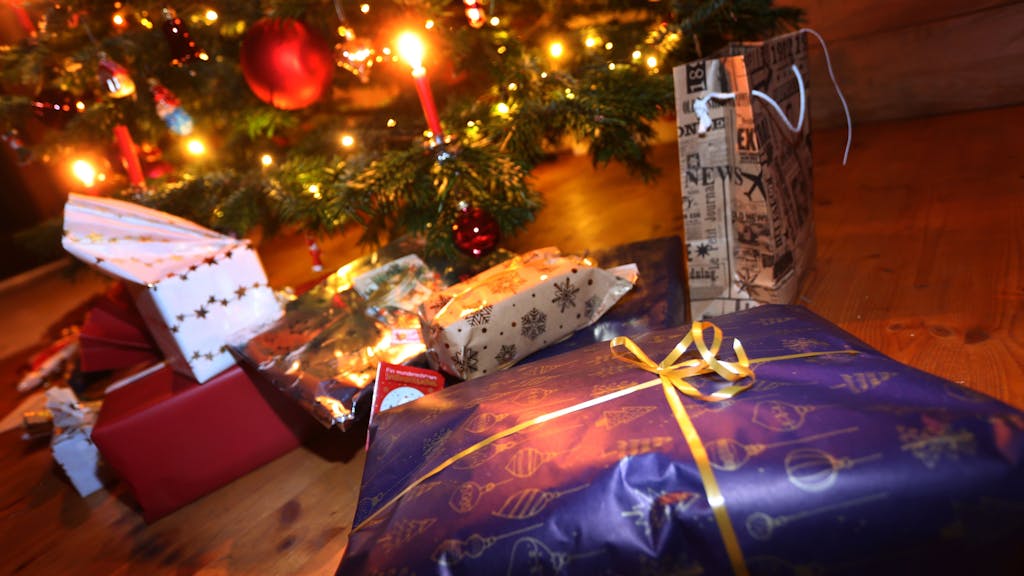 Verpackte Geschenke liegen in einem Wohnzimmer unter einem festlich geschmücktem Weihnachtsbaum.&nbsp;