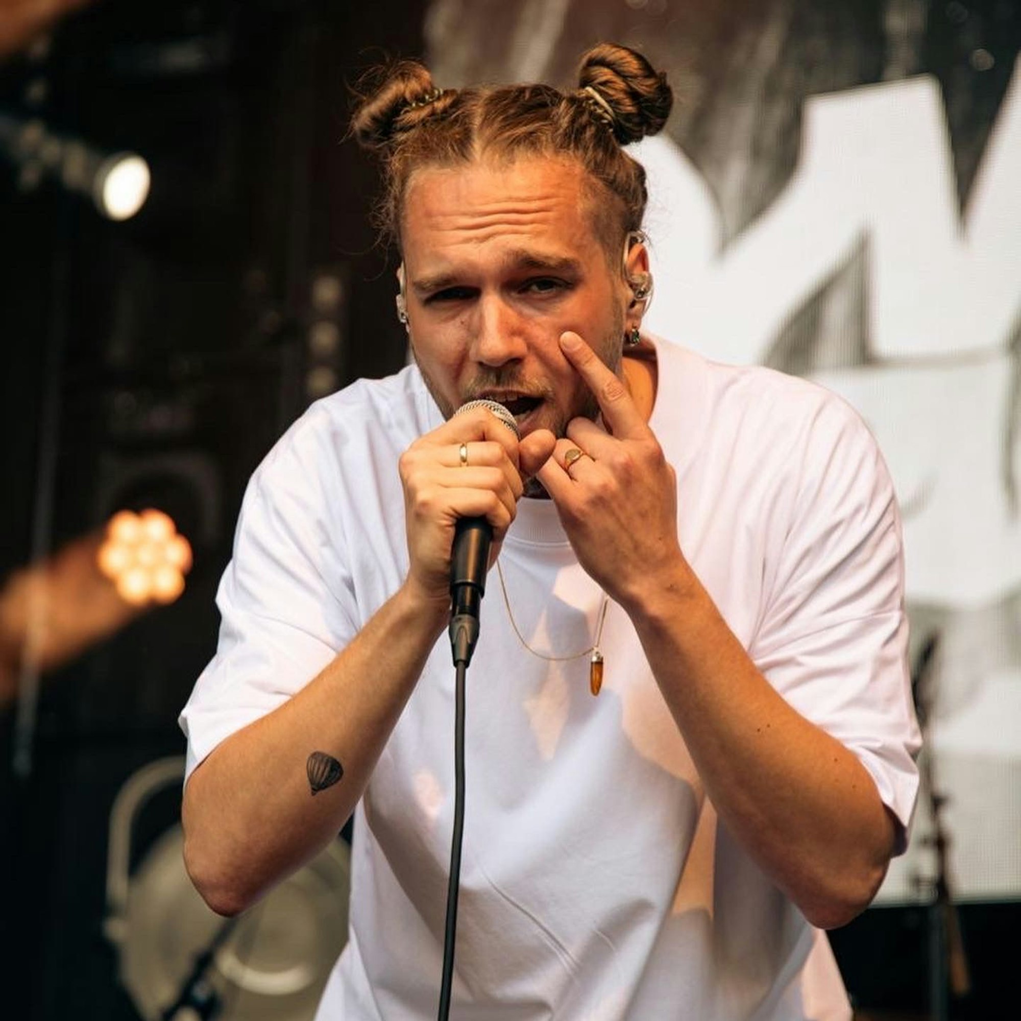 Sänger Wunso trägt ein weißes T-Shirt. Er steht auf einer Bühne und singt in ein Mikrofon, das er in der Hand hält.