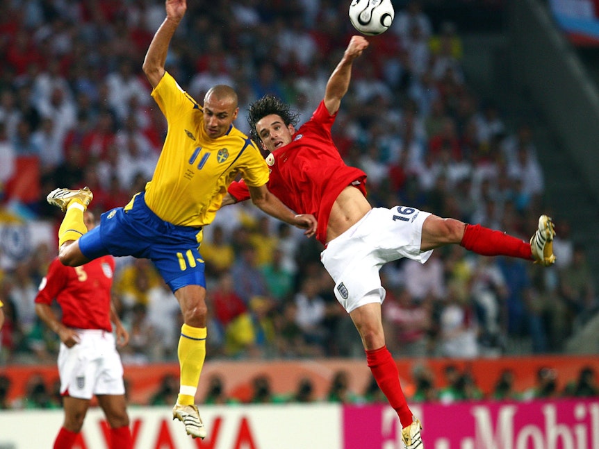 Henrik Larsson und Owen Hargreaves kämpfen bei einem Fußballspiel um den Ball. Beide fliegen regelrecht durch die Luft.