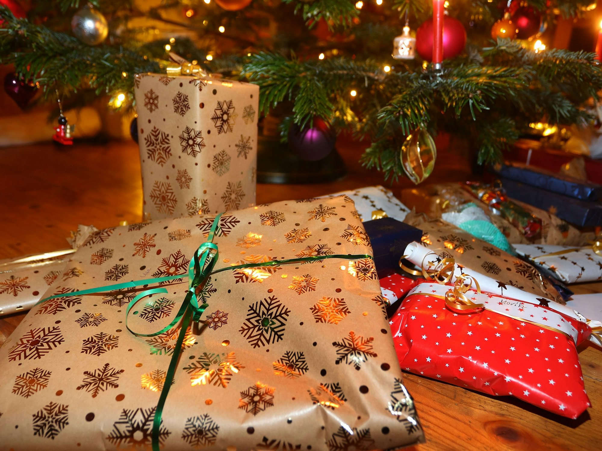 Verpackte Geschenke liegen in einem Wohnzimmer unter einem festlich geschmücktem Weihnachtsbaum.