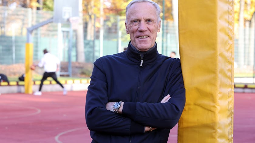 Der Kölner Sportprofessor Ingo Froböse steht auf einem Sportplatz und guckt in die Kamera.