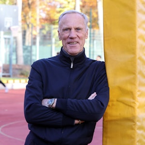Der Kölner Sportprofessor Ingo Froböse steht auf einem Sportplatz und guckt in die Kamera.