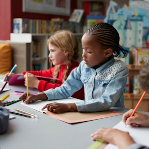Drei Schulkinder sitzen in einem Klassenraum, in der Mitte ein schwarzes Mädchen.