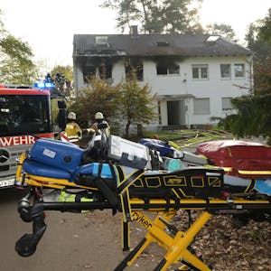 Rauch strmöt aus Fenster der Notunterkunft in Bergisch Gladbach, davor steht ein Feuerwehr und eine Bare mit Gegenständen darauf.