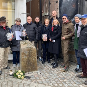 Künstler Gunter Demnig (l.) steht neben der Stele vor dem früheren Synagogenstandort in Bad Münstereifel. An ihrem Fuß sind weiße Rosen abgelegt. Unter den Teilnehmern der Aktion ist auch die Bad Münstereifeler Bürgermeisterin Sabine Preiser-Marian (4.v.r.).