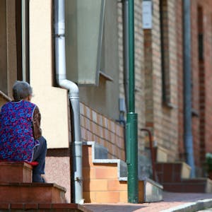 Ein ältere Frau sitzt auf der Treppe vor ihrem Wohnhaus.