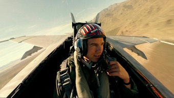 Tom Cruise als Captain Pete „Maverick“ Mitchell in „Top Gun: Maverick“. Er sitz in einem Flieger und spricht in ein Mikrofon an seiner Kleidung.