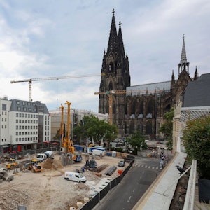 Blick aus südlicher Richtung auf den Kölner Dom, vor dem sich eine riesige Baustelle befindet, auf der das neue Laurenz-Carré entstehen soll. Baustellenfahrzeuge, Kräne und Bagger arbeiten auf der Baustelle.