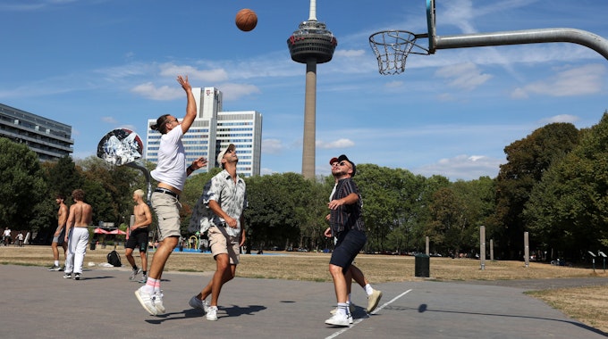 Mehrere junge Männer spielen Basketball auf einem Basketballplatz am Grüngürtel.
