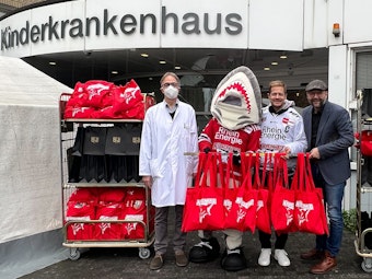 Professor Michael Weiß, Sharky, KEC-Kapitän Moritz Müller sowie Haie-Geschäftsführer Philipp Walter mit den Geschenken vor der Kinderklinik.