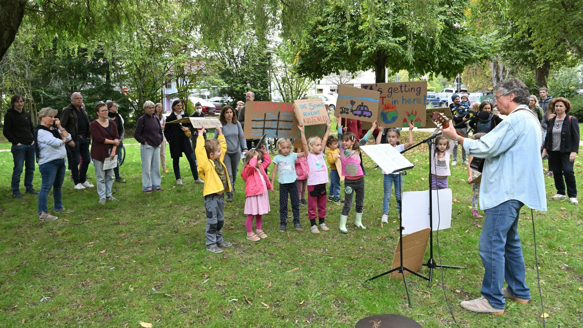 Auf einer Fridays for Future Demo in Rösrath halten Kinder Plakate hoch und ein Mann spielt Gitarre. Eltern stehen im Hintergrund.