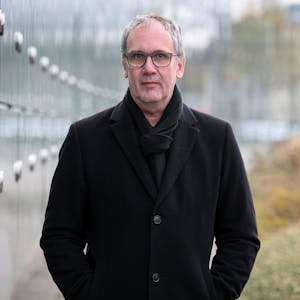 Bestseller-Autor Volker Kutscher steht in einem schwarzen Mantel vor dem Neven-DuMont-Haus