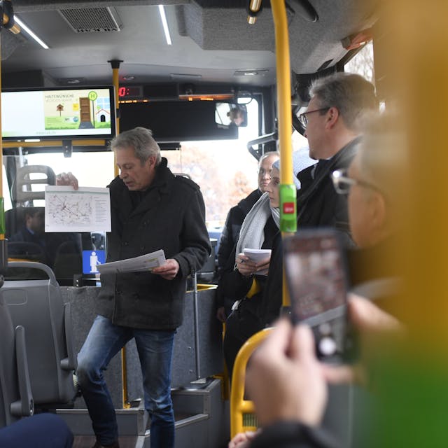 Andreas Glodowski steht in einem Kleinbus und hält einen ausgedruckten Fahrplan hoch, während er das neue Zülpicher ÖPNV-Konzept vorstellt.
