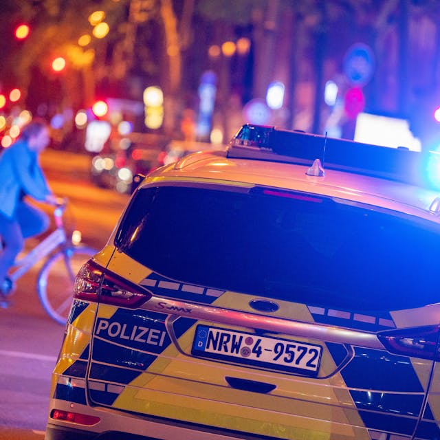 Ein Polizei-Auto in blau-gelber Lackierung fährt über eine Straße in Köln, es ist mit Blaulicht unterwegs. (Symbolbild)