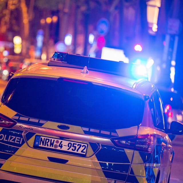 Ein Polizei-Auto in blau-gelber Lackierung fährt über eine Straße in Köln, es ist mit Blaulicht unterwegs. (Symbolbild)